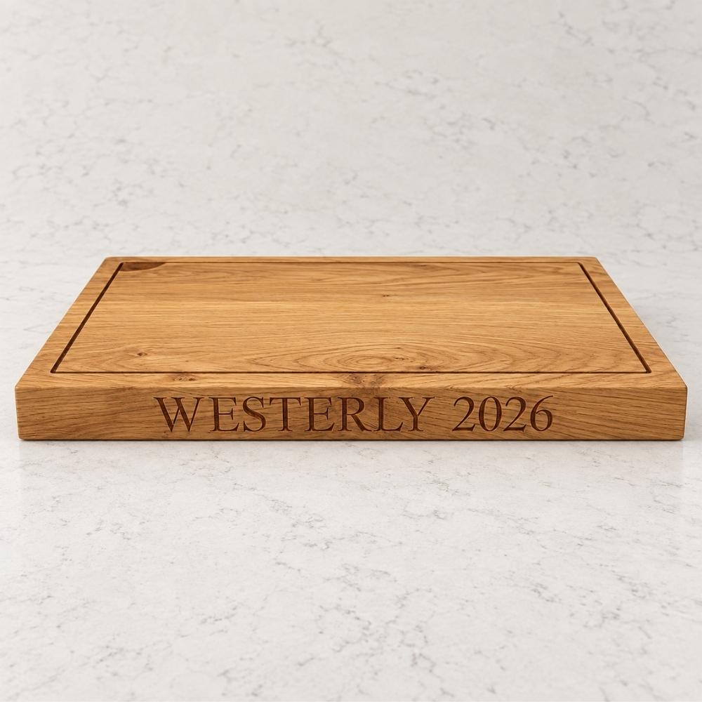 A rectangular wooden serving board with engraved text reading 'WESTERLY 2026' on the front, photographed on a light marble-like surface.