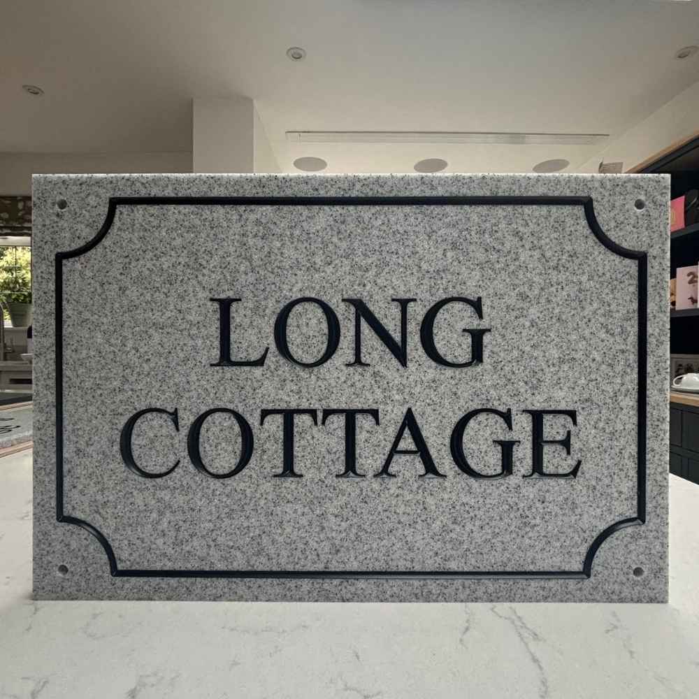 A rectangular granite sign with rounded corners and the words 'LONG COTTAGE' in large black serif letters, displayed indoors on a light marble surface.