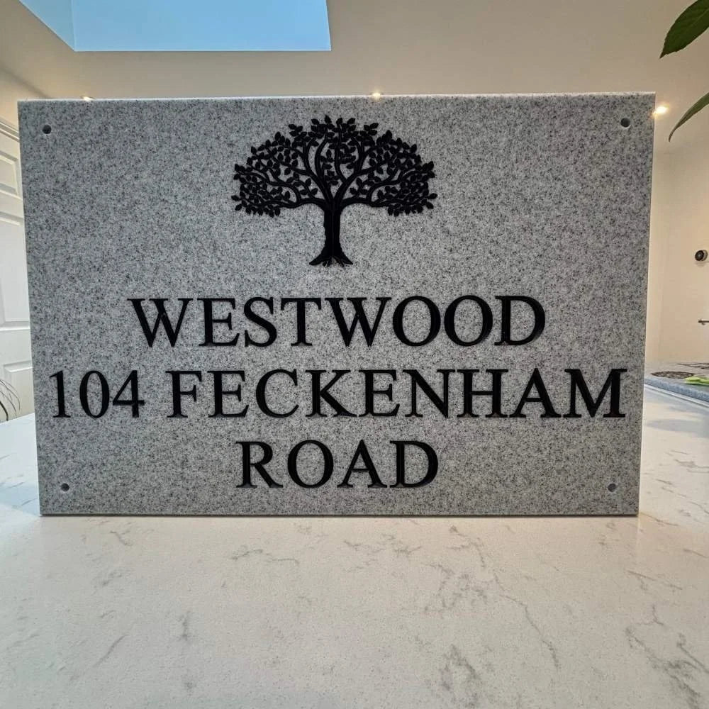 Gray stone plaque with tree design and text 'WESTWOOD 104 FECKENHAM ROAD' on a marble surface.