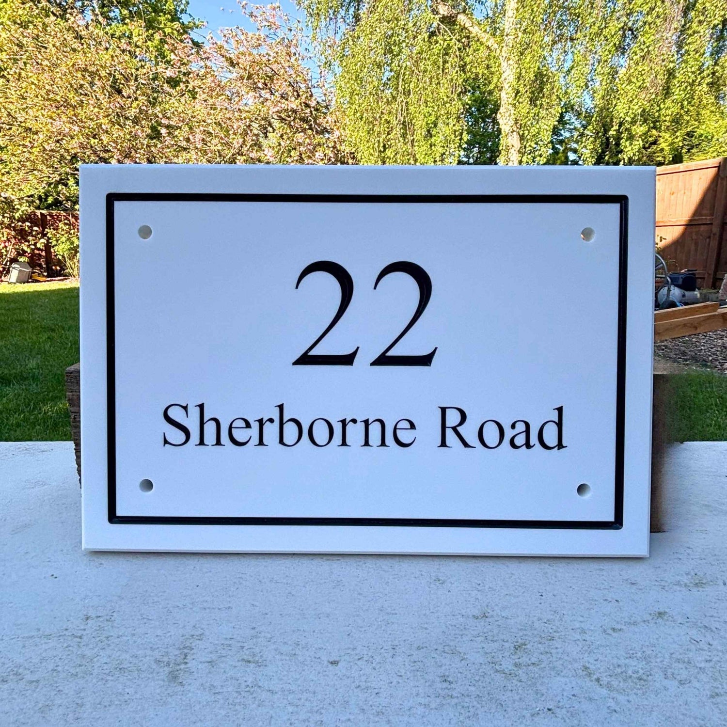 House number sign '22 Sherborne Road' on a white background with trees in the background.