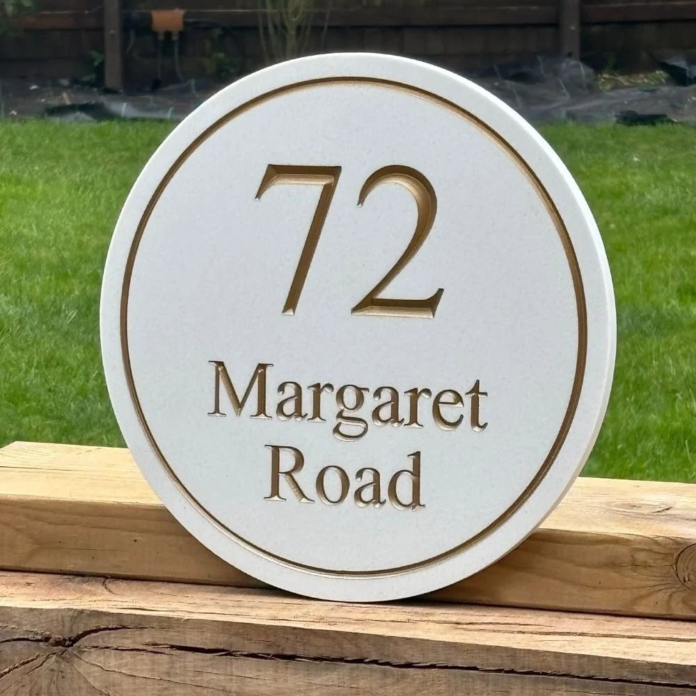 Round Quartz house number sign with '72 Margaret Road' on a wooden surface with grass in the background