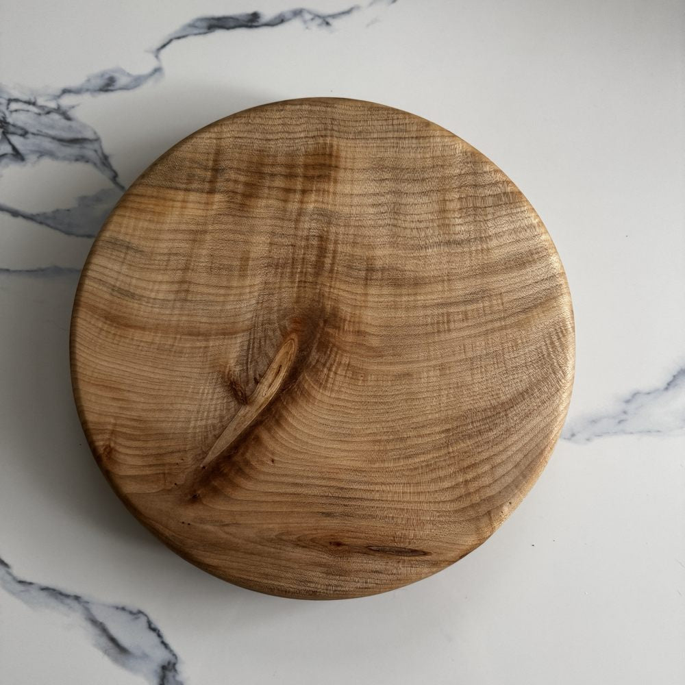 A round wooden serving board with a natural grain pattern, photographed from directly above on a white marble surface.