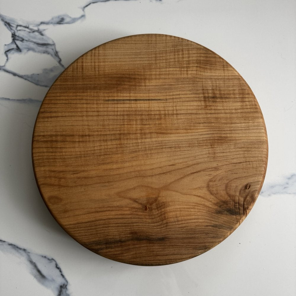 A round wooden cutting board with a natural grain pattern, photographed from directly above on a white marble surface.