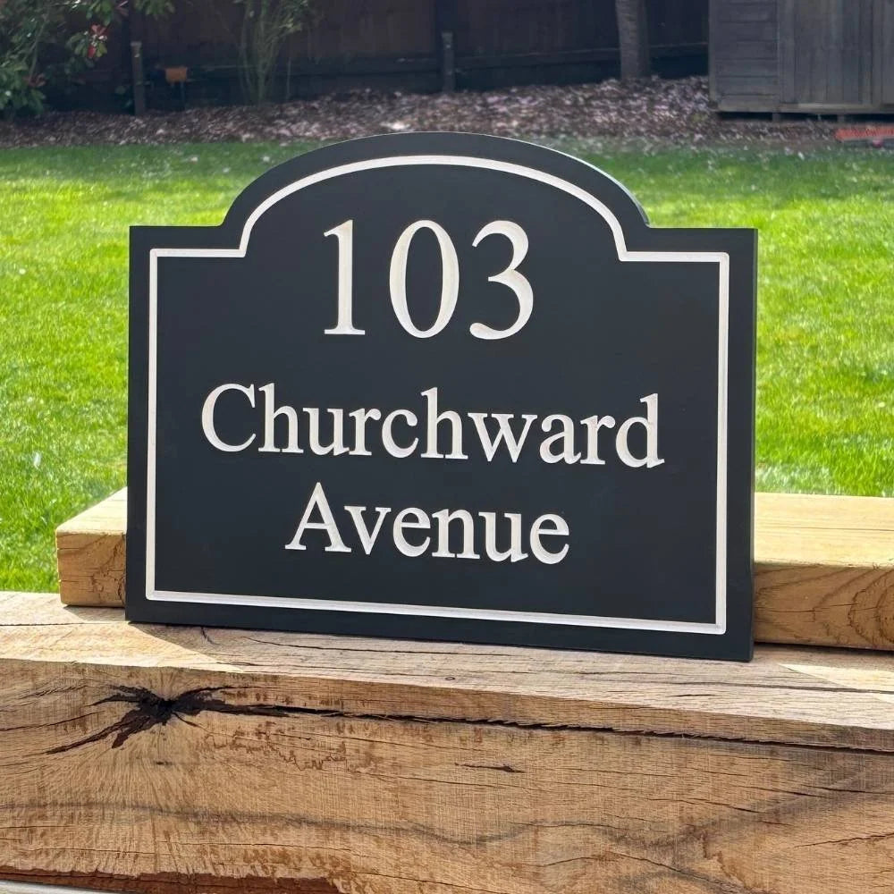 House number sign '103 Churchward Avenue' on a wooden surface with grass in the background