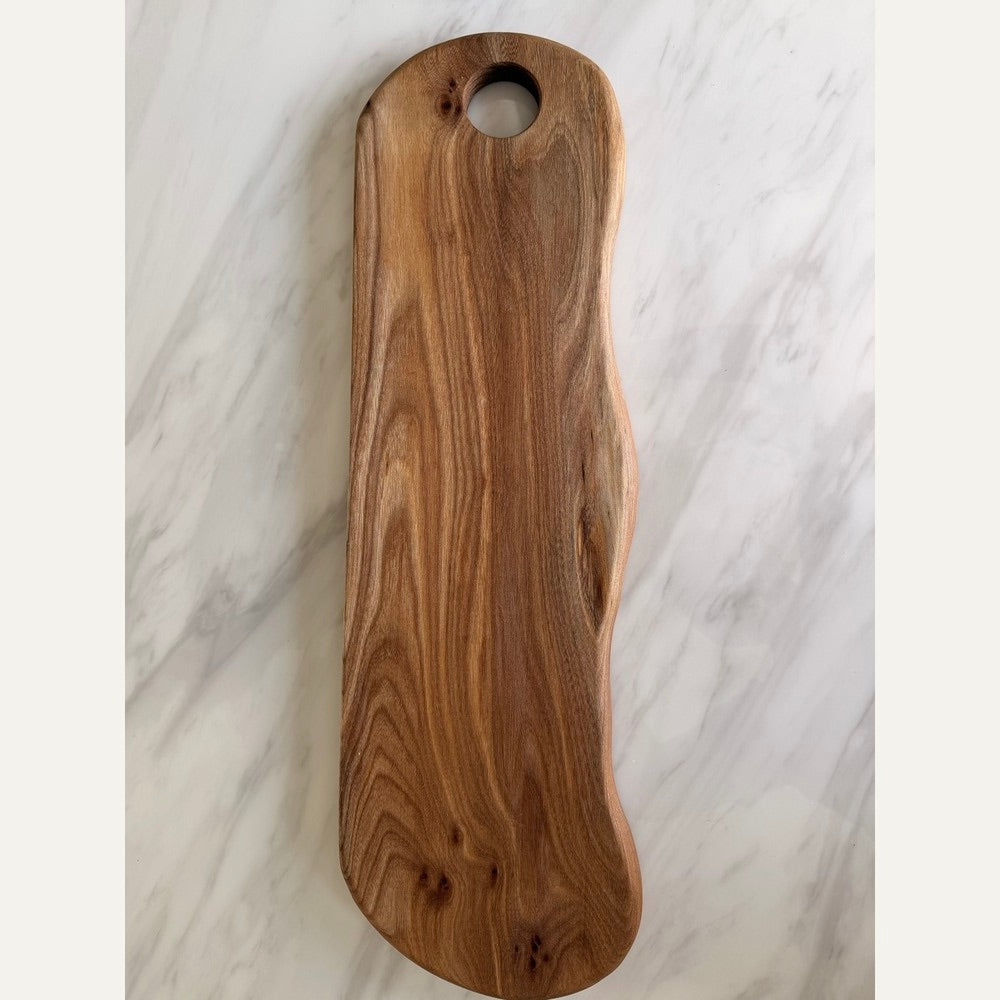 A long, hand-shaped wooden serving board with a natural grain pattern and a circular hole near the top, displayed on a white marble surface.