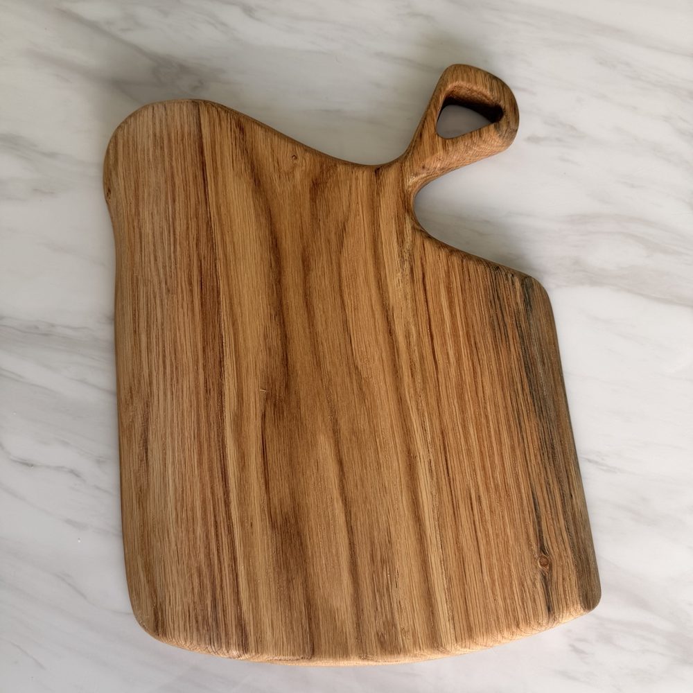 A rectangular wooden cutting board with a rounded handle, shown from a top-down view on a white marble surface.