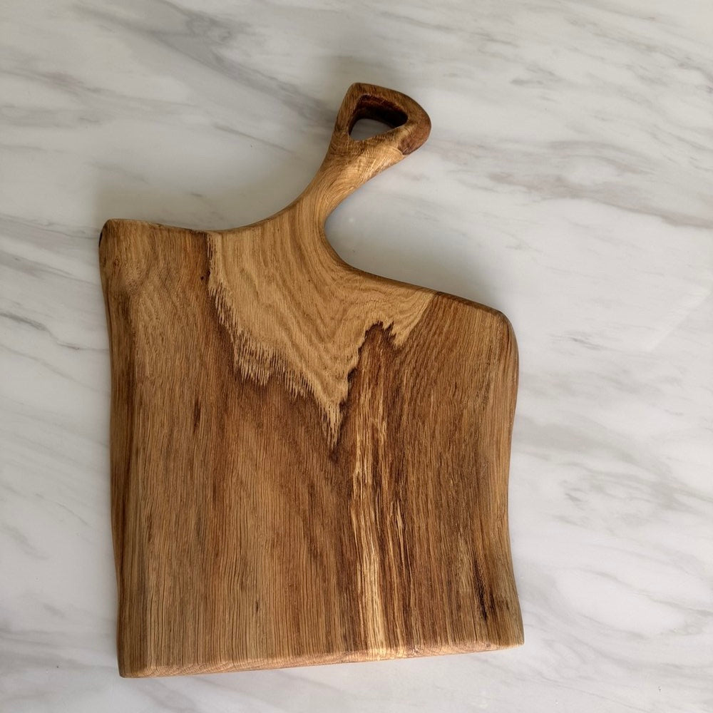 A rustic wooden serving board with a handle, displayed on a white marble surface.