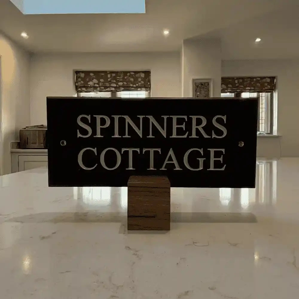 Sign reading 'Spinners Cottage' in a modern interior setting with marble floor and neutral walls.