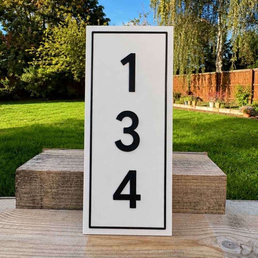 A vertical Quartz sign with black border and large black numbers '1 3 4' on a wooden table outdoors, with grass, trees, and a fence in the background.