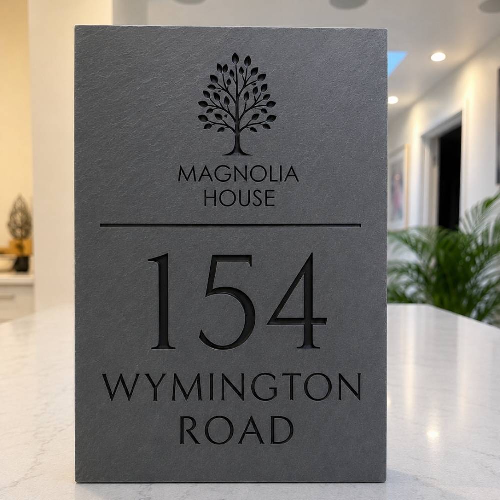 A rectangular dark grey slate sign for Magnolia House, 154 Wynington Road, standing on a light marble countertop in a modern interior setting.