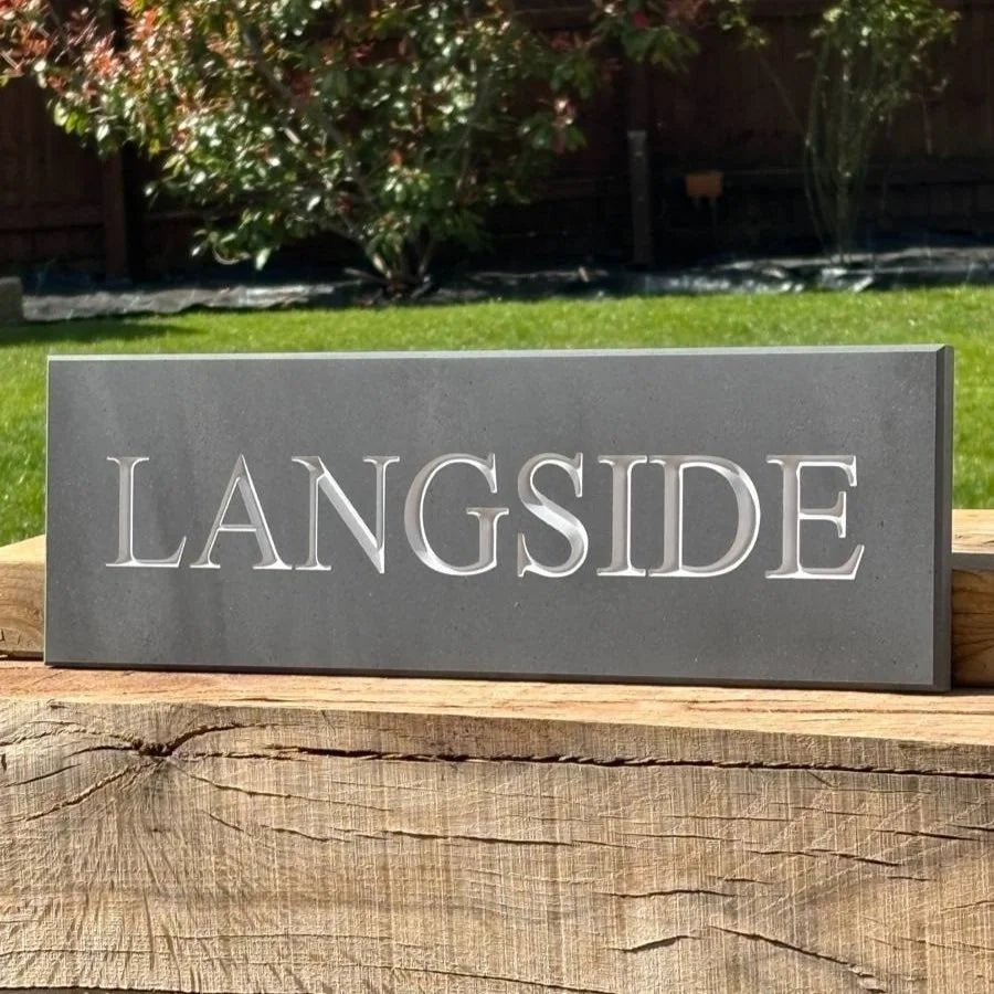 Gray rectangular sign with 'LANGSIDE' engraved on it, placed on wooden planks outdoors.